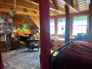 A cozy cabin interior with a bed, desk, and wheelchair, featuring wooden walls and large windows.
