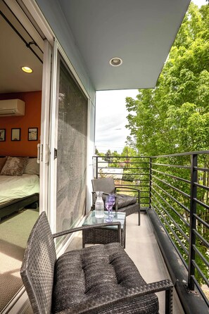 A balcony with a glass table and wicker chairs, overlooking a garden and a building. - Private Rooftop w Grill, AC + Free Parking (Seattle)