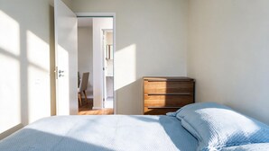 A bedroom with a bed, a wooden dresser, and a door leading to another room. - Apto c Piscina e Varanda Perto do Parque Ol Mpico (Rio de Janeiro)