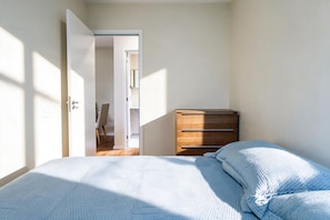 A bedroom with a bed, a wooden dresser, and a door leading to another room. - Apto c Piscina e Varanda Perto do Parque Ol Mpico (Rio de Janeiro)