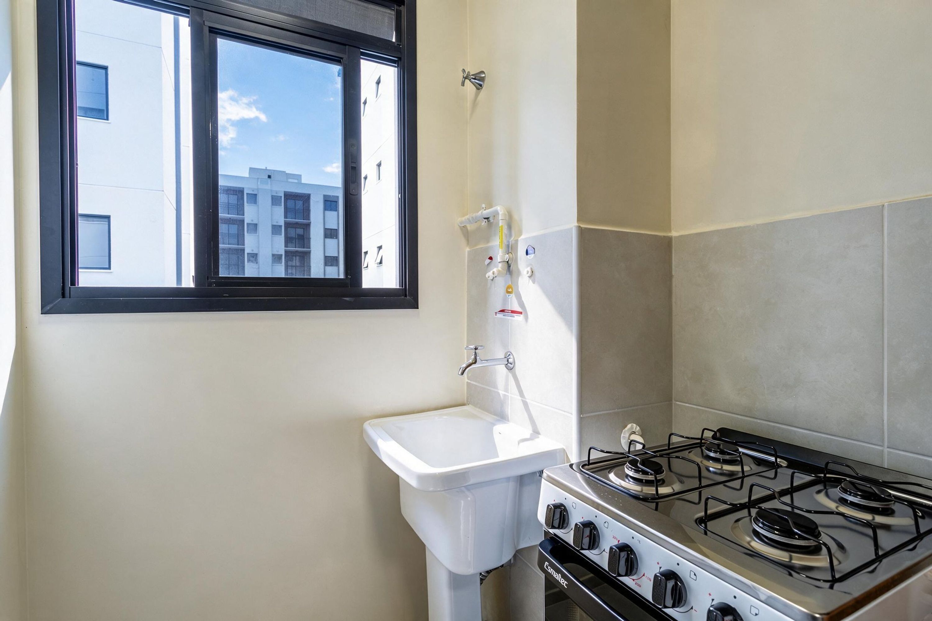 Una cocina con estufa a gas, un fregadero y ventana con vista a un edificio.