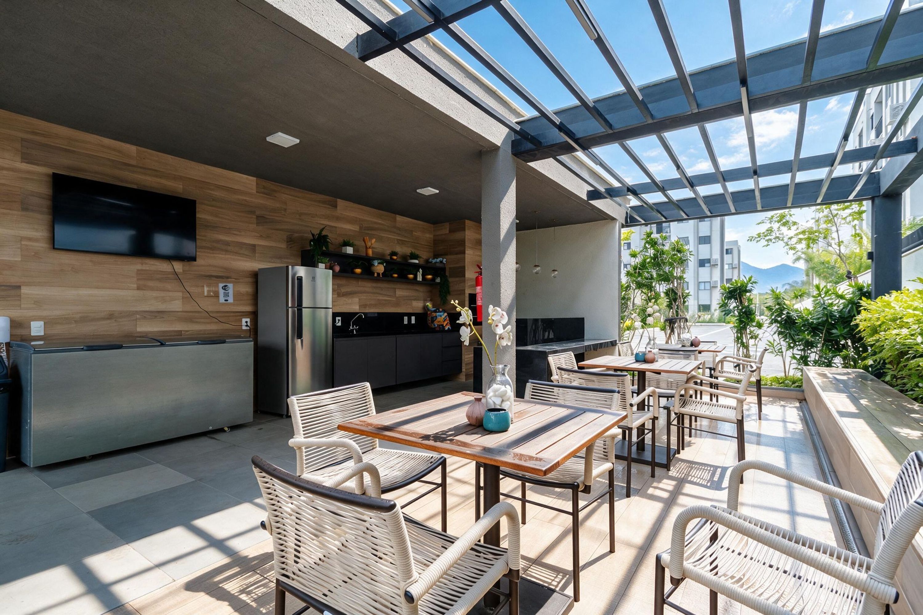 Una cocina exterior moderna con un muro de madera, electrodomésticos integrados y un comedor con sillas y mesas de mimbre.
