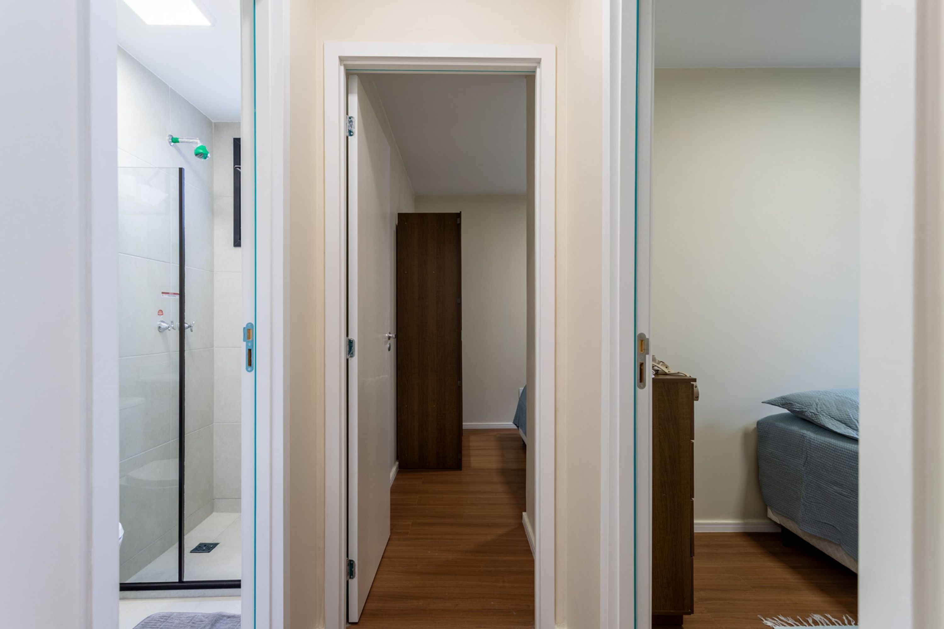 Un pasillo que conduce a un dormitorio con cama, un armario de madera y una cabina de ducha de vidrio.
