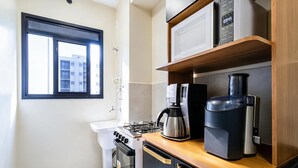 A compact kitchen with a gas stove, a coffee maker, and a microwave on a wooden countertop. - Apto c Piscina e Varanda Perto do Parque Ol Mpico (Rio de Janeiro)