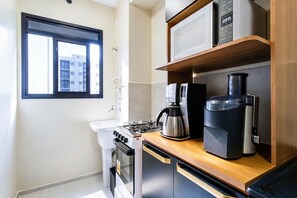 A compact kitchen with a gas stove, a coffee maker, and a microwave on a wooden countertop. - Apto c Piscina e Varanda Perto do Parque Ol Mpico (Rio de Janeiro)