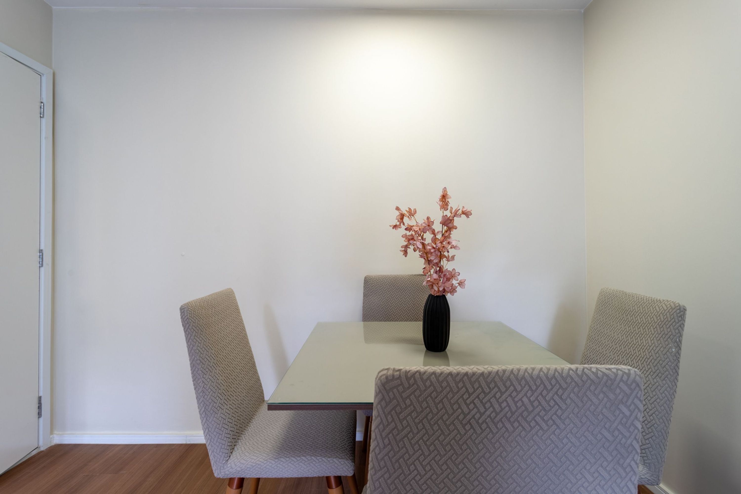 Uma área de refeições com uma mesa, cadeiras e um vaso com flores.