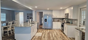 A modern kitchen with white cabinetry, a central island, and a stainless steel refrigerator. - Waterfront! 3/3 Home on canal w/firepit & grill
3 Bedrooms • 3 Bath • 7 Beds  (Hudson)