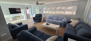 Ein modernes Wohnzimmer mit Sofa, Sesseln, Couchtisch und Fernseher.