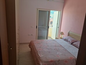 A bedroom with a bed, a nightstand, a lamp, a sliding door to an outdoor area, and a door leading to another room.