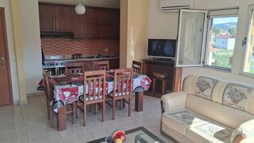 Ein Wohnzimmer mit Sofa, ein Essbereich mit Tisch und Stühlen, eine Küche mit Schränken und Herd sowie ein Fernseher auf einem Schrank.