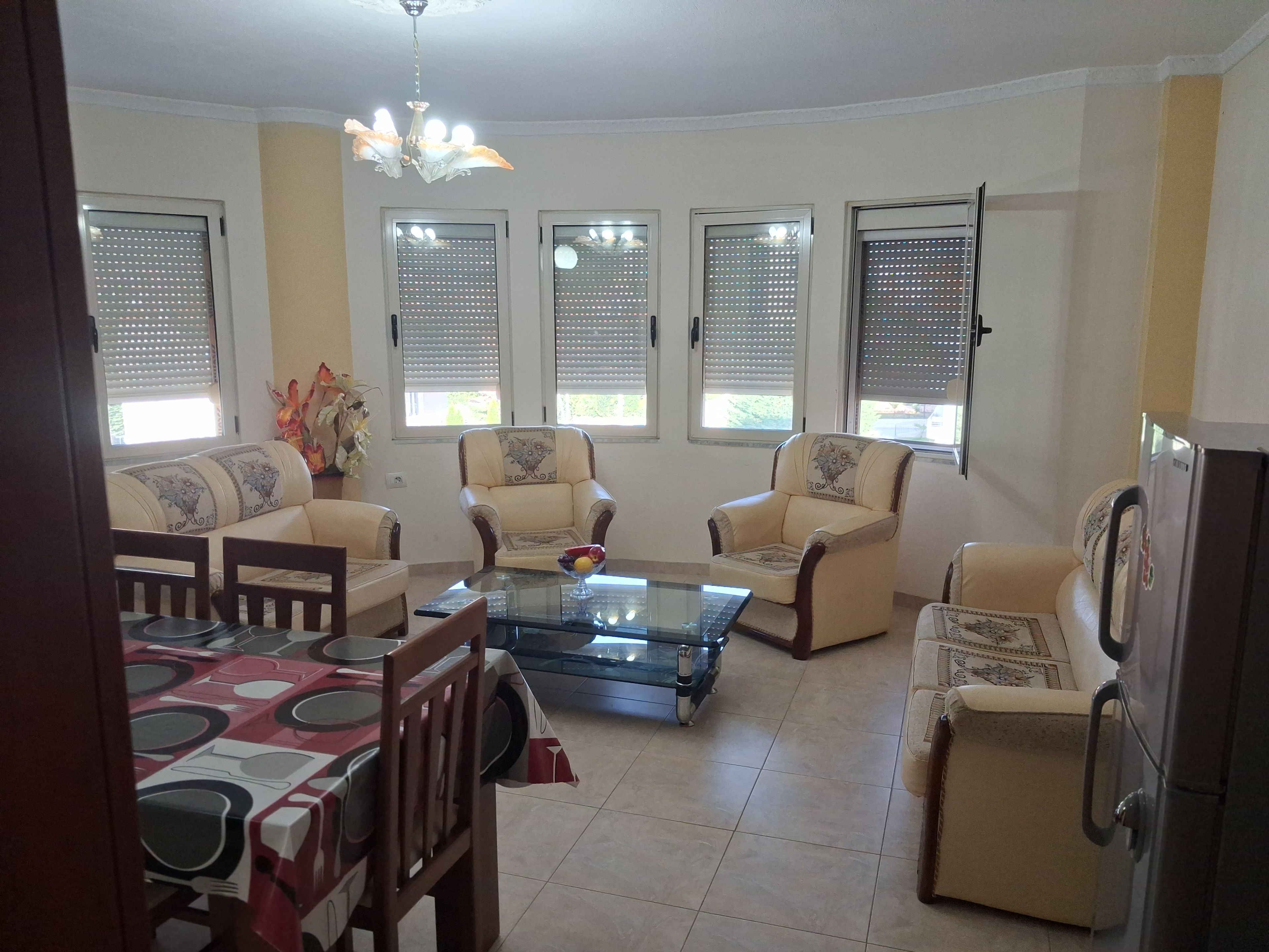 A living room with a glass coffee table, two armchairs, a sofa, and a dining table with chairs.