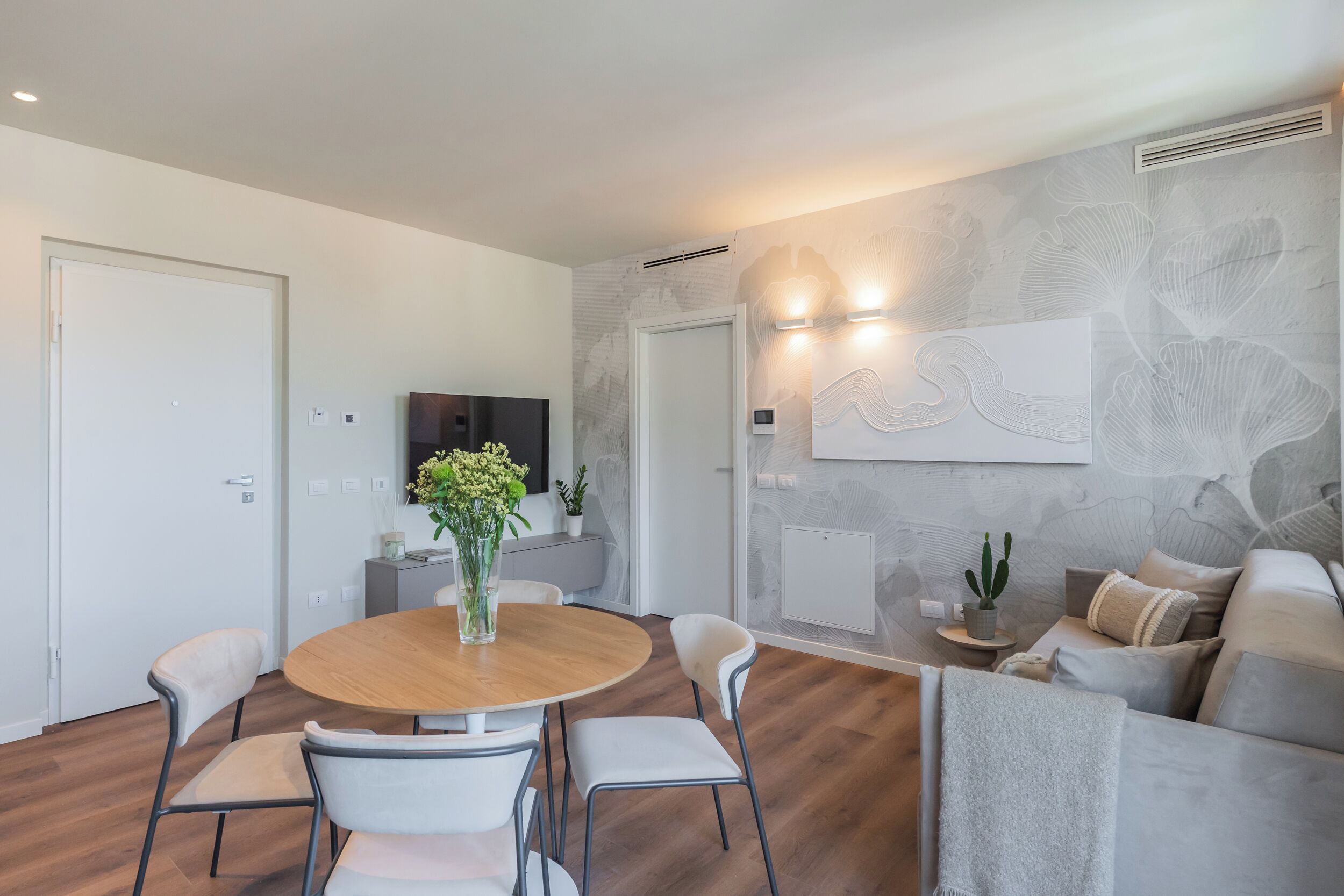 Ein modernes Wohnzimmer mit einem runden Esstisch, weißen Stühlen, einer Couch und einem flachbildfernseher an der Wand.