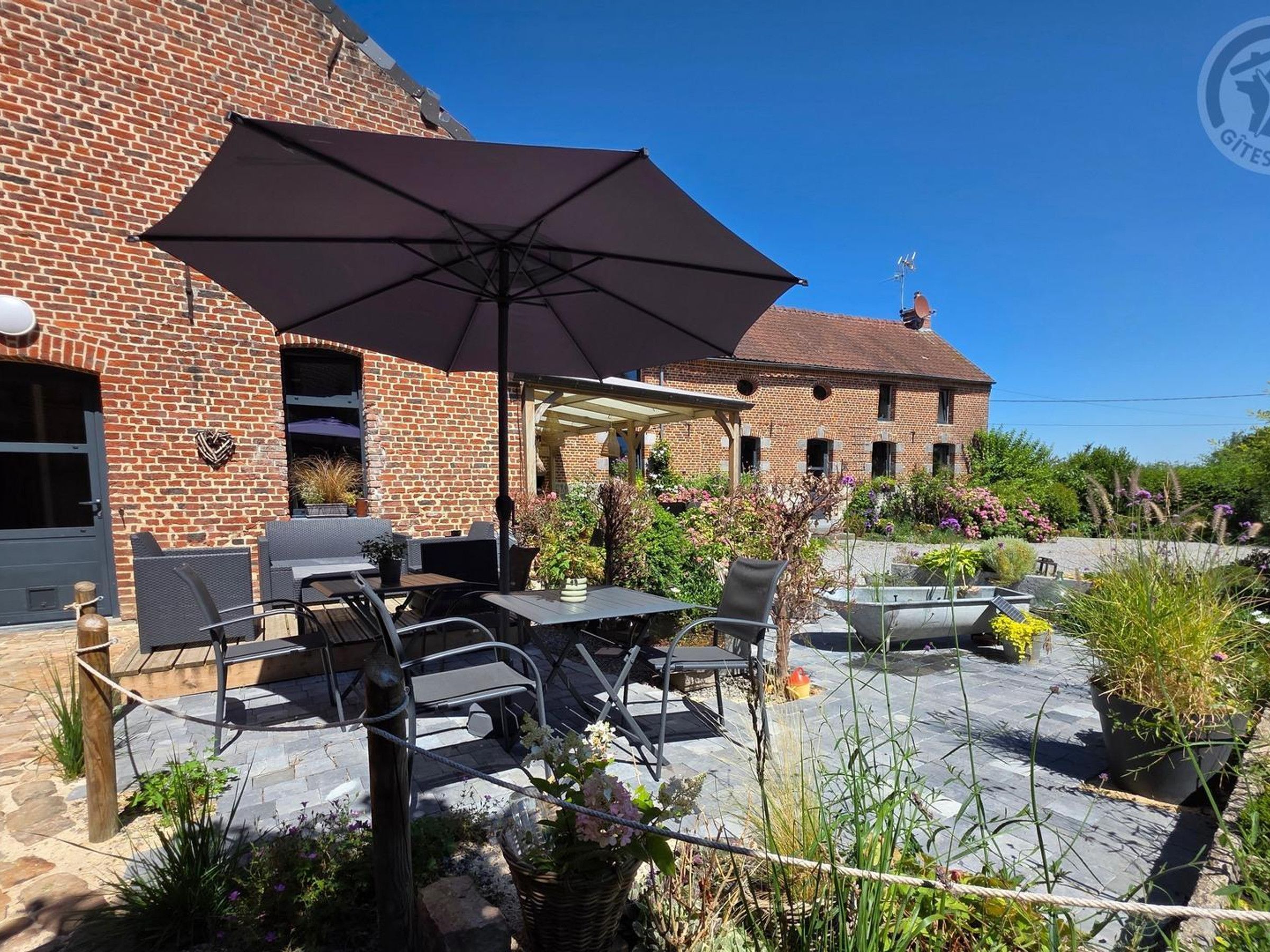 An outdoor patio with a brick building, outdoor furniture, and a large umbrella.