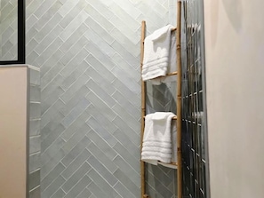 A bathroom with a herringbone patterned tile wall, a wooden towel rack, and a glass shower enclosure.
