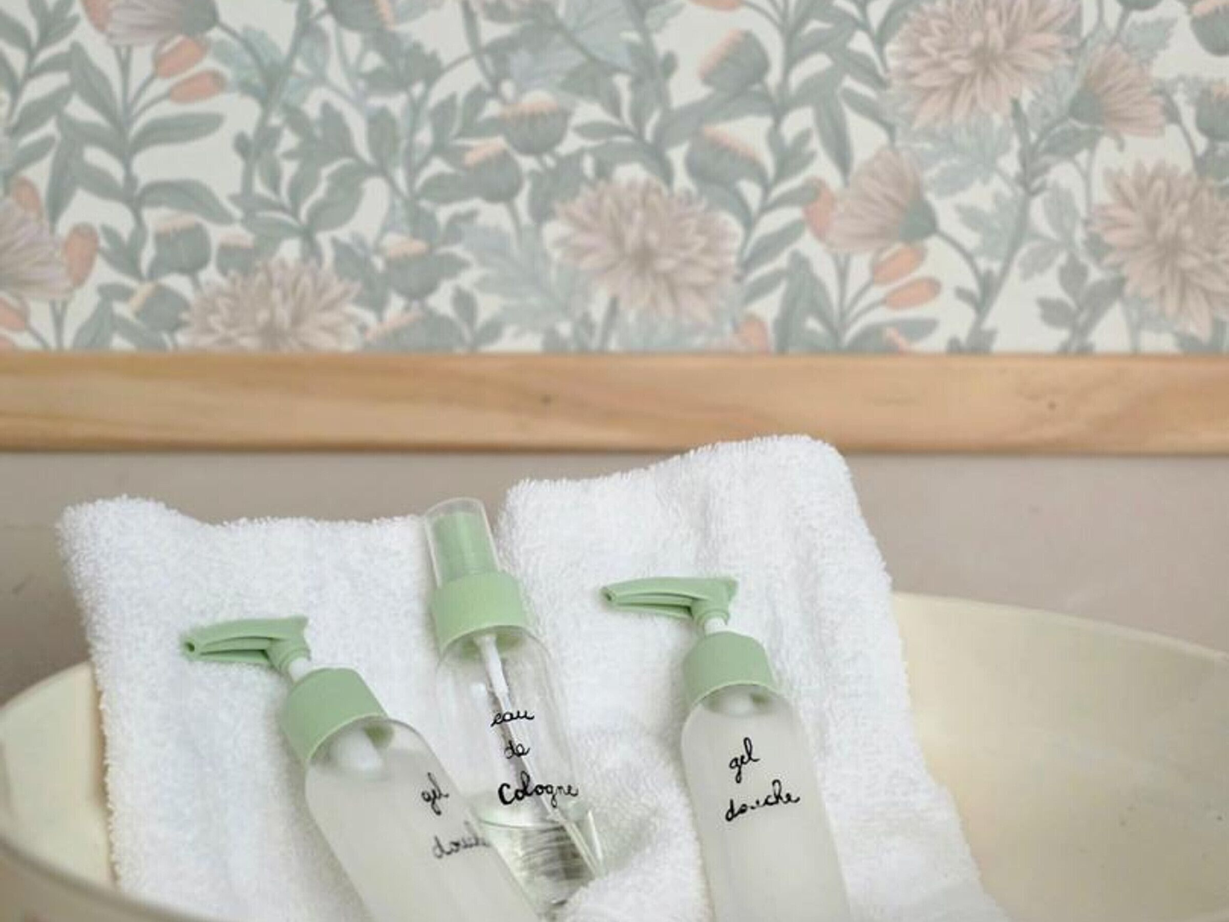 Ein Badezimmer mit blumigem Tapetenmuster, einem weißen Handtuch und drei Gelflaschen.