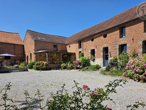 A courtyard with a brick building, a covered seating area, and a gravel path.