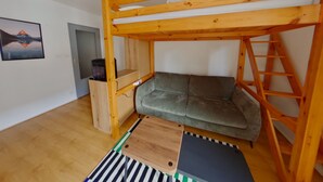 A bunk bed with a wooden frame, a grey sofa, a small wooden table, and a striped rug. - Central apartment with wifi - 4 guests (Les Rousses)