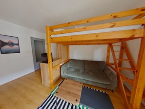 Ein Stockbett mit Holzrahmen, eine graue Schlafcouch, ein kleiner Holztisch und ein Streifenmuster-Teppich.