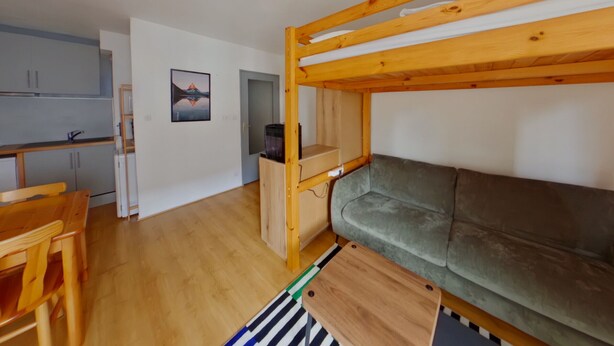 A bunk bed with a green mattress, a wooden desk with a chair, a kitchenette with cabinets, and a framed picture on the wall. - Central apartment with wifi - 4 guests (Les Rousses)