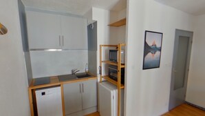A compact kitchen with a dishwasher, a sink, and a small refrigerator. There is a wooden shelf unit with a television and a framed picture on the wall. - Central apartment with wifi - 4 guests (Les Rousses)
