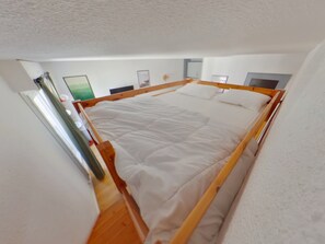 Ein Zimmer mit einem Bett, einem hölzernen Kopfteil, weißen Wänden und einer Tür.