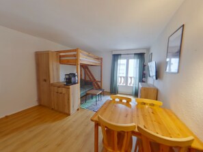 A compact room with a bunk bed, a small kitchenette, a dining table with chairs, and a view of the outside through a window. - Central apartment with wifi - 4 guests (Les Rousses)
