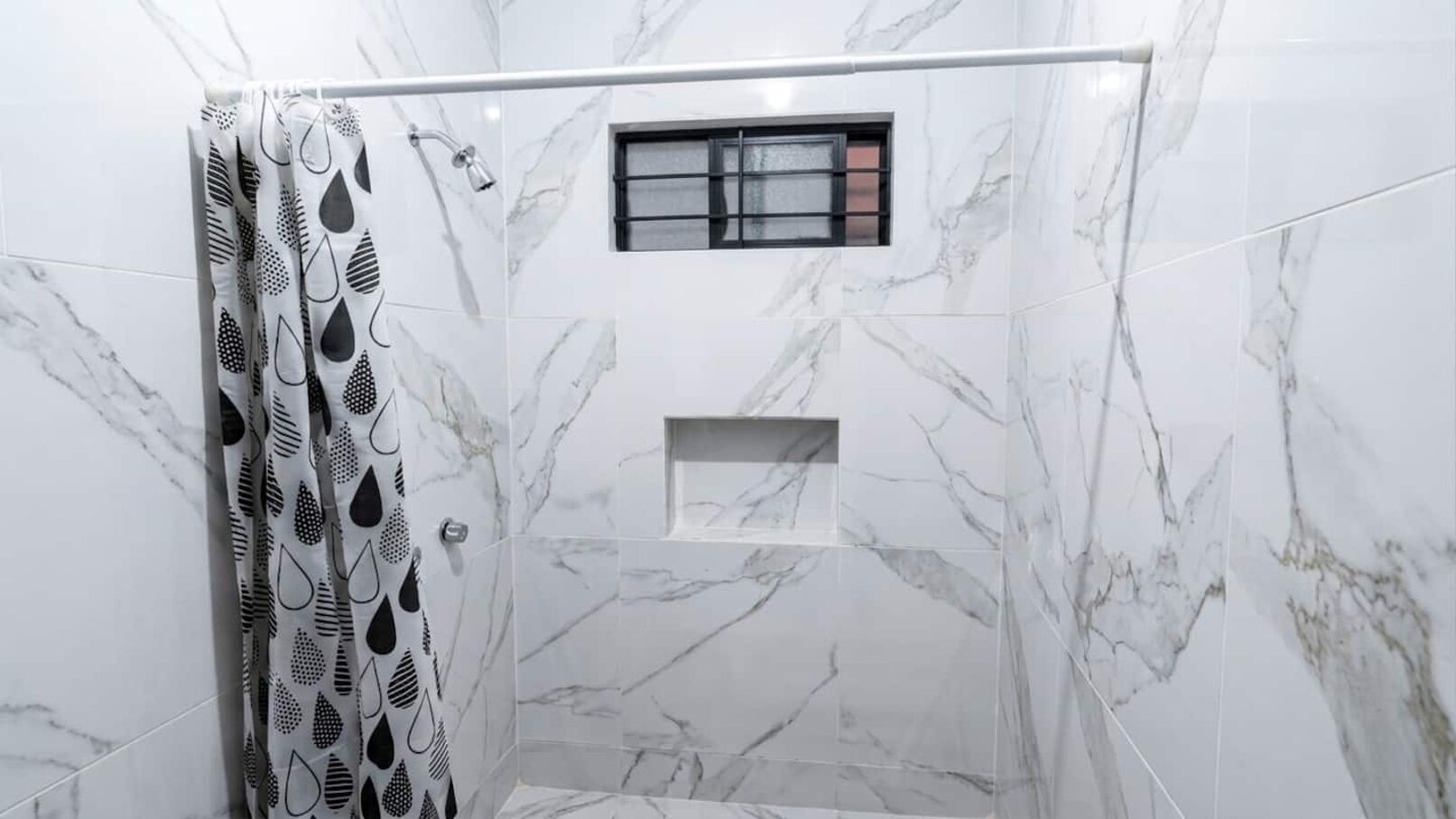 A shower area with a marble wall, a window, and a shower curtain with a leaf pattern.