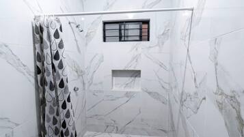 A shower area with a marble wall, a window, and a shower curtain with a leaf pattern.