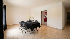 A dining area with a table set for four, chairs, a vase with flowers, and a kitchen visible through an open doorway.