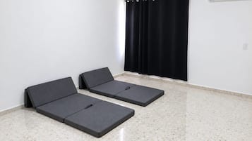 Et rum med to mørke madrasser på et prikket gulv, en sort gardin og en hvid væg med en central aircondition.