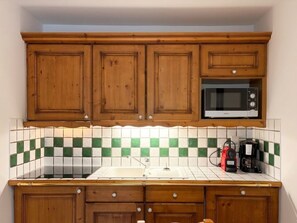 A kitchen with wooden cabinets, a microwave, a sink, and a tiled backsplash. - Comfortable apartment with open view - 4 guests (Les Menuires)