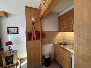 Eine kompakte Küche mit Holzausstattung, einem Spülbecken und einer kleinen Mülltonne.