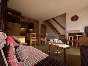 A cozy living area with a sofa, wooden dining table, chairs, and a staircase. - Cozy apartment, pets welcome, near slopes - 5 guests (Méribel)