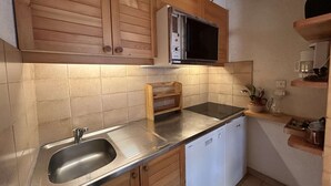 A compact kitchen with wooden cabinets, a microwave, a built-in oven, a stainless steel sink, and a dishwasher. - Cozy apartment, pets welcome, near slopes - 5 guests (Méribel)