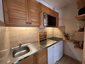 Eine kompakte Küche mit Holzausstattung, einer Mikrowelle, einem Backofen, einer Edelstahlspüle und einem Geschirrspüler.