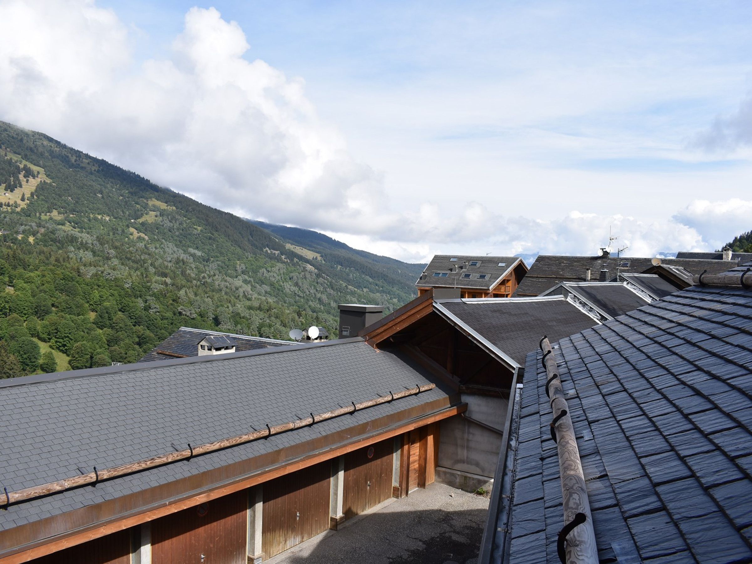 A residential building with multiple roof levels, satellite dishes, and a mountainous backdrop.