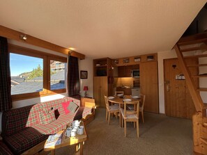 Ein gemütliches Zimmer mit einer Couch, einem Esstisch, Stühlen, einer Küchenzeile und einem Fenster mit Blick.