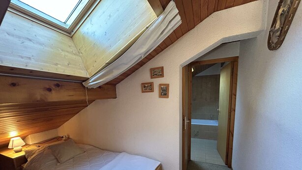 A bedroom with a skylight, a bed, a nightstand, and a bathroom visible through an open door. - Cozy apartment, pets welcome, near slopes - 5 guests (Méribel)