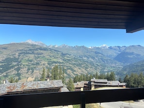 Blick auf Berge vom Balkon mit Holzbalkon, mit Ausblick auf ein Tal mit Häusern und einer Bergkette.