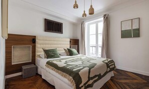 Un dormitorio con una cama grande, una ventana con cortinas, una rejilla en la pared y un cuadro enmarcado.