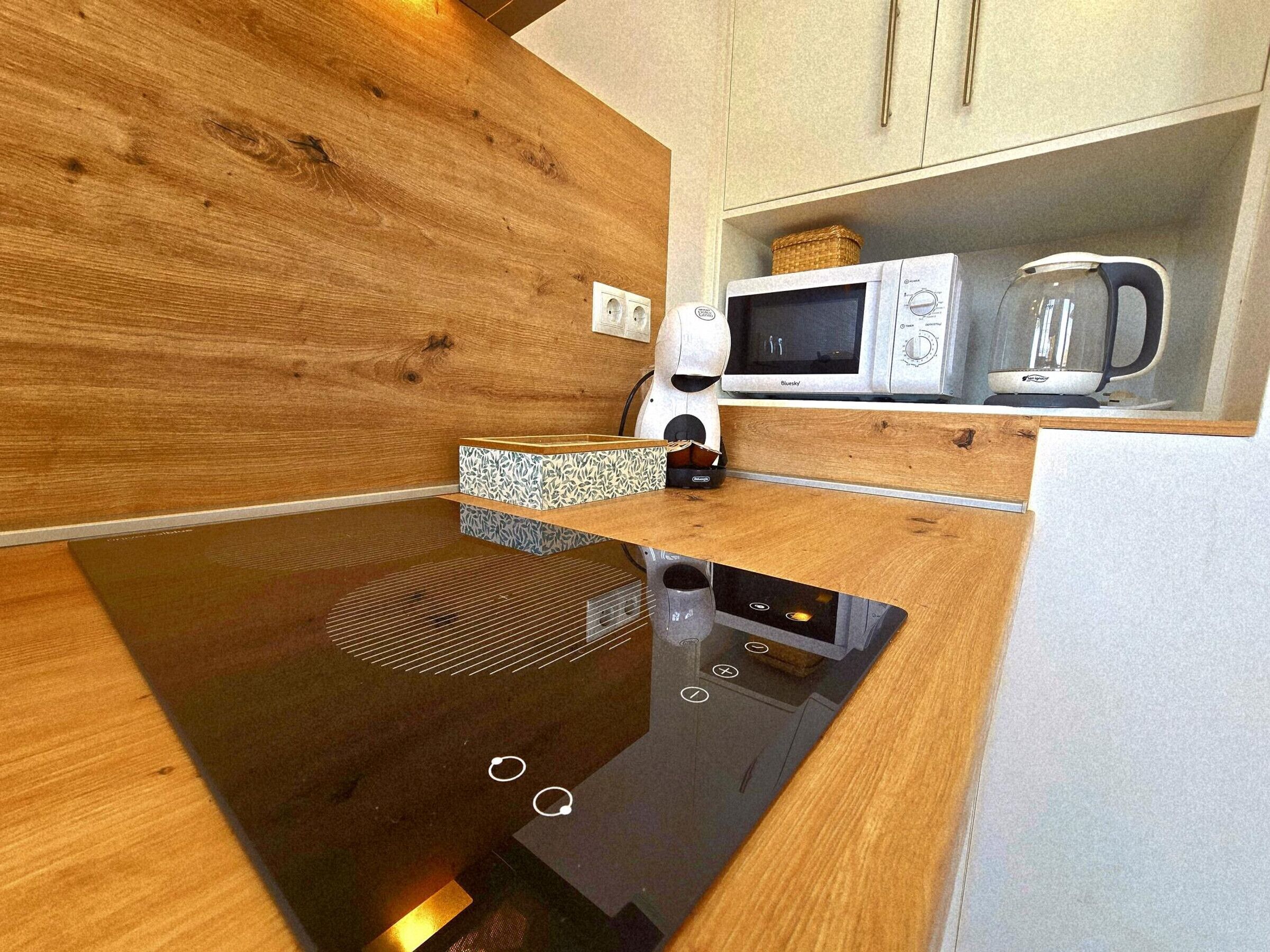 A modern kitchen with a wooden countertop, a microwave, a kettle, and a built-in oven.