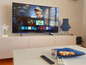 Ein Fernseher, der die Londoner Tennismeisterschaften zeigt, eine Fernbedienung, ein Smartphone und eine dekorative Schale auf einem Tisch.