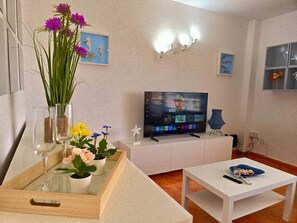 A modern living room with a flat-screen TV, a coffee table, and a glass-top table with flowers. - Lidia Apartment 1: Seafront in La Carihuela (Torremolinos)