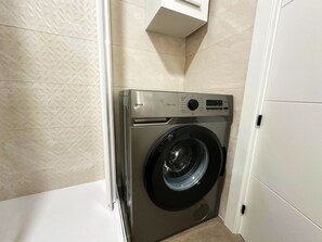 Ein kompakter, moderner Waschraum mit einer Frontlader-Waschmaschine, einer Steuerungseinheit und einem kleinen Schrank darüber.