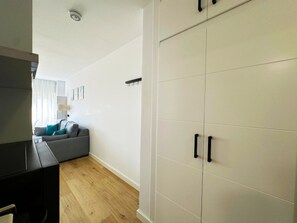 Ein modernes Wohnzimmer mit einem grauen Sofa, Holzboden und einem weißen Kleiderschrank mit schwarzen Griffen.