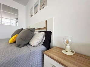 Ein Schlafzimmer mit einem Bett, Kissen, einem Nachttisch, einer Lampe und einem Fenster.