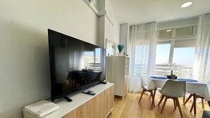 A modern living room with a flat-screen TV, a dining area with a table and chairs, and a view of the city through large windows. - Central seaview studio with pool in Torremolinos (Torremolinos)