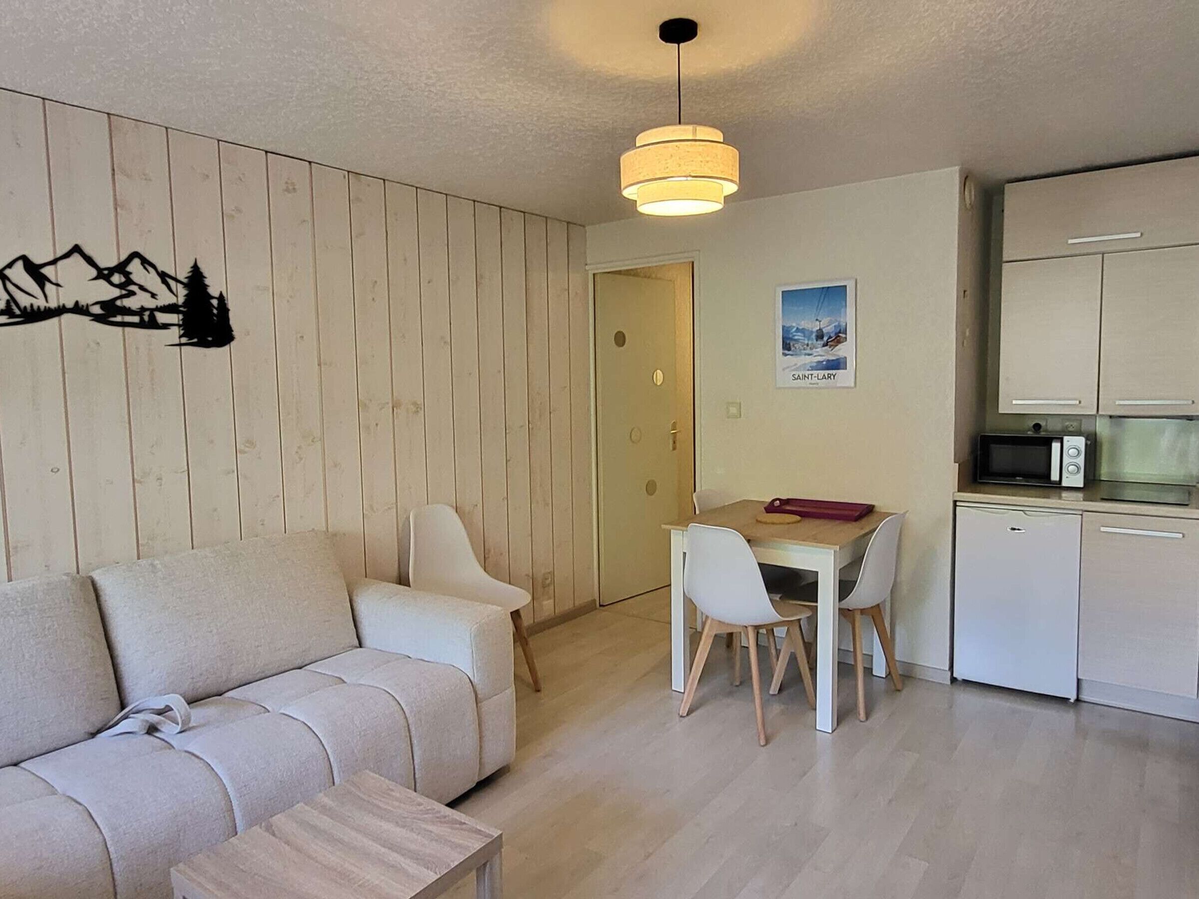 A compact living space with a sofa, dining table, chairs, a kitchenette, and a wall-mounted light fixture.