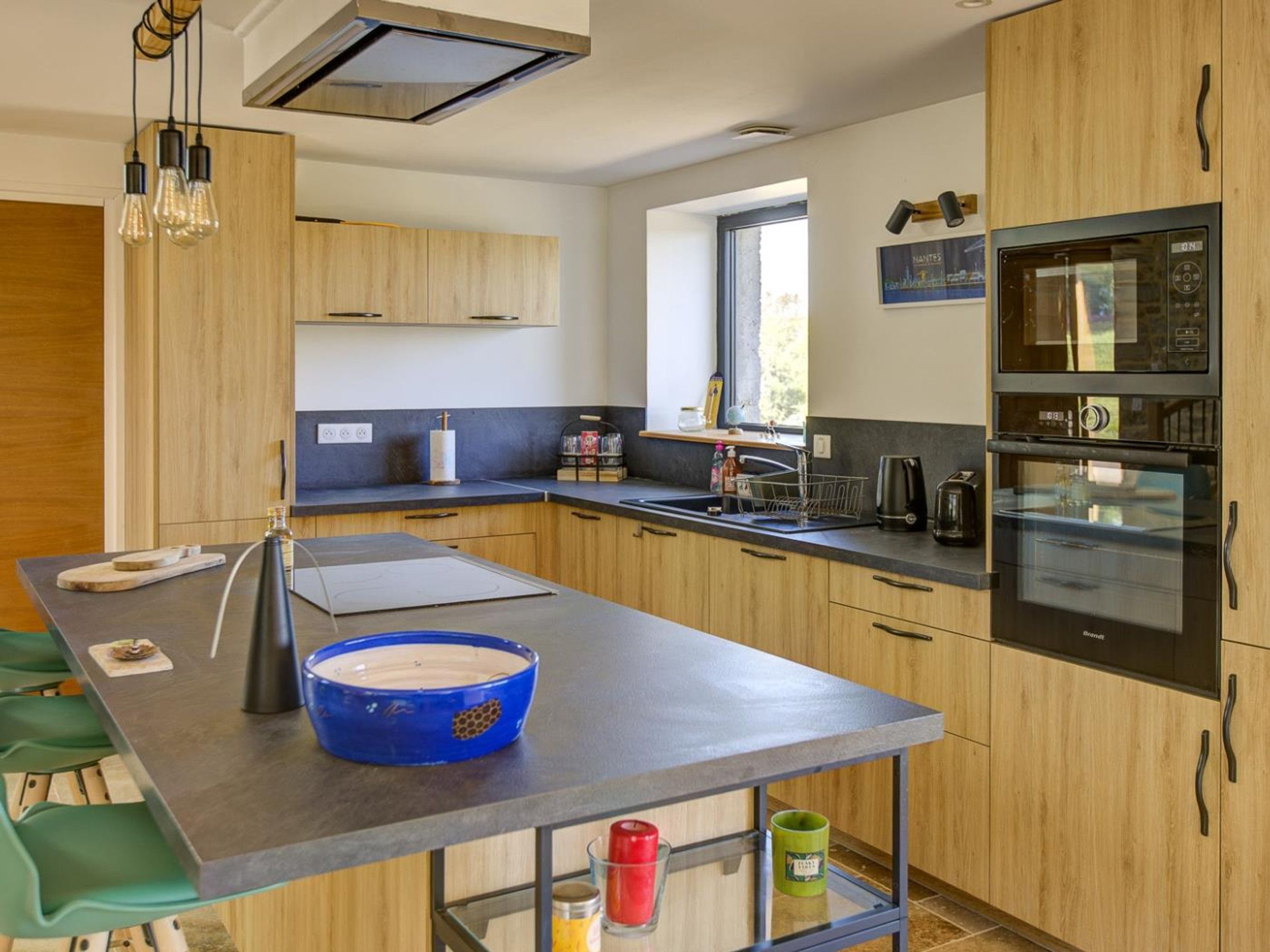 Una cucina moderna con mobili in legno, una grande isola e elettrodomestici integrati, tra cui un forno a microonde e un forno.