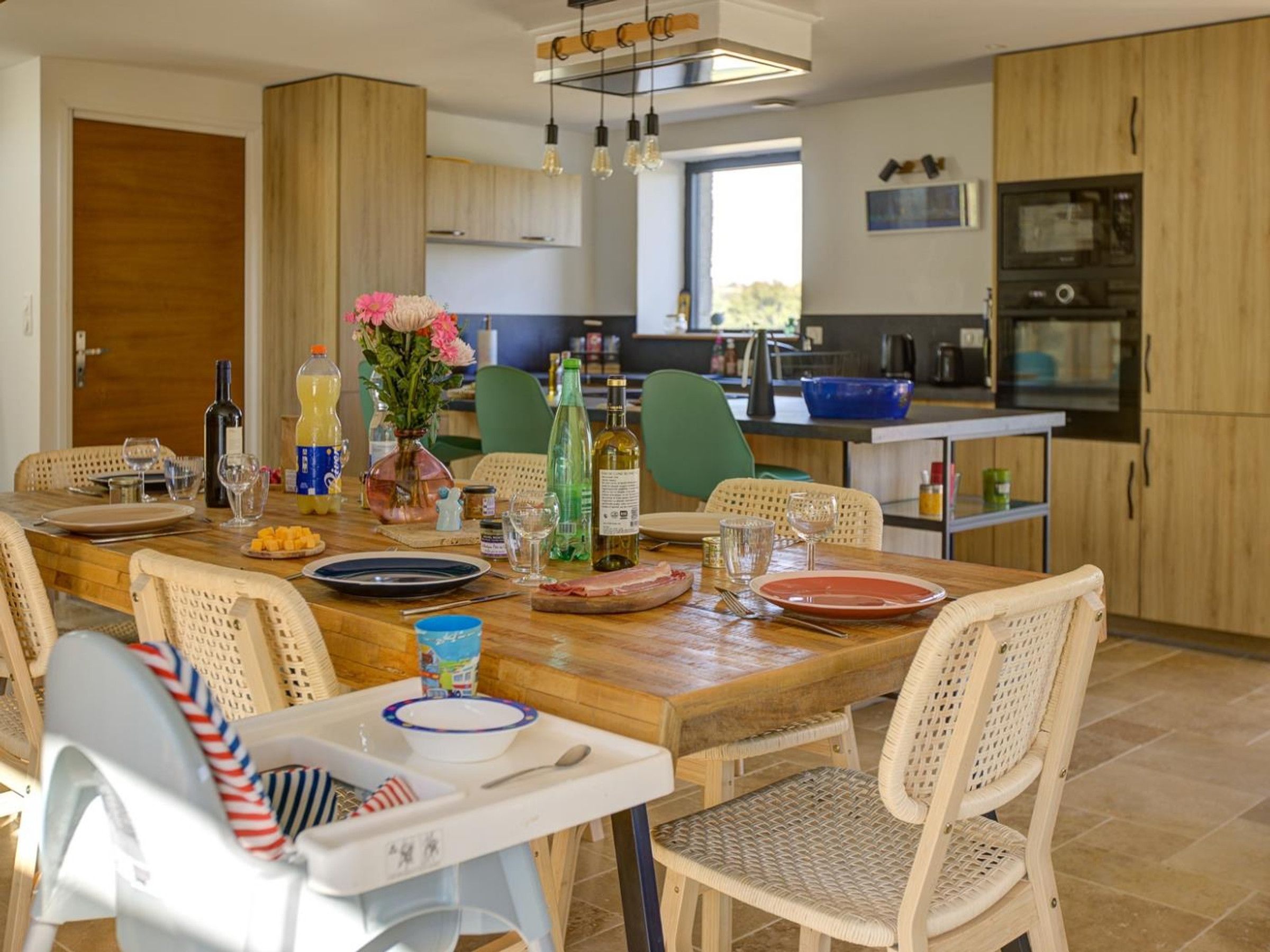 A dining area with a wooden table, wicker chairs, and a baby high chair.